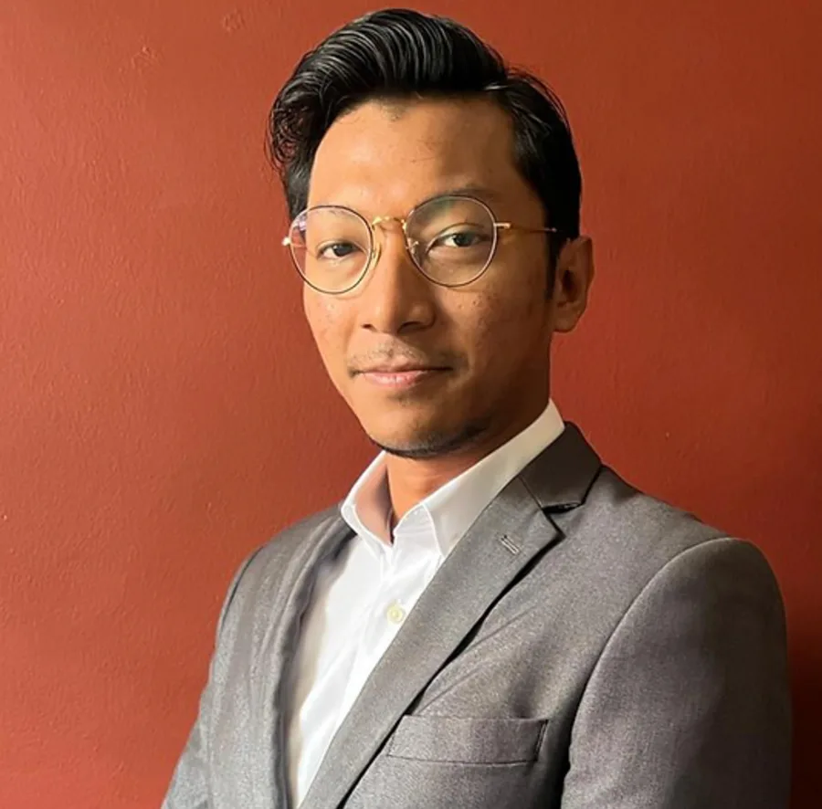 Person in gray suit smiling against red wall.