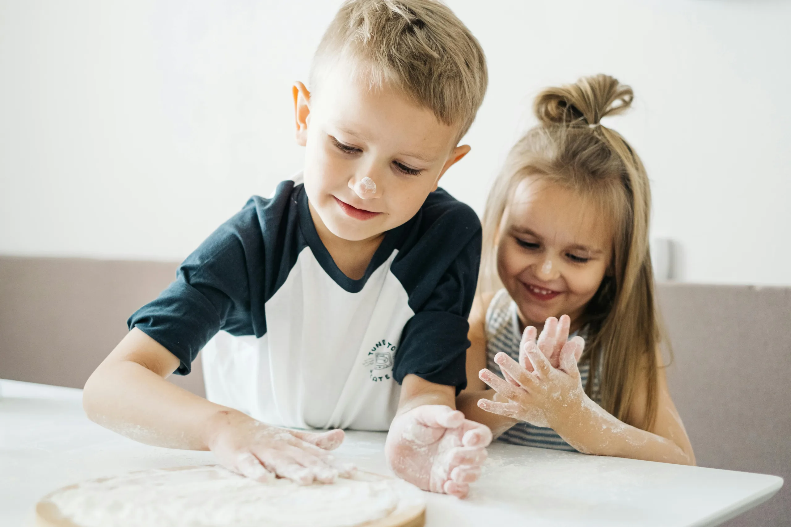 Kids happily making dough together in kitchen.