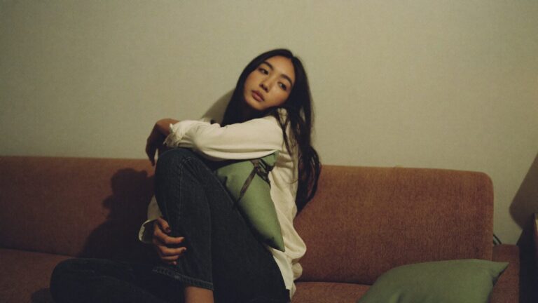 Seorang wanita muda memeluk kusyen di atas sofa pada waktu malam, menggambarkan perasaan cemas