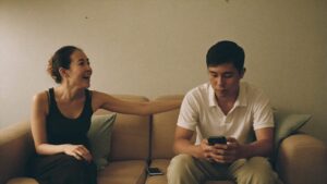 A woman speaking to her partner on a sofa while he looks down at his phone