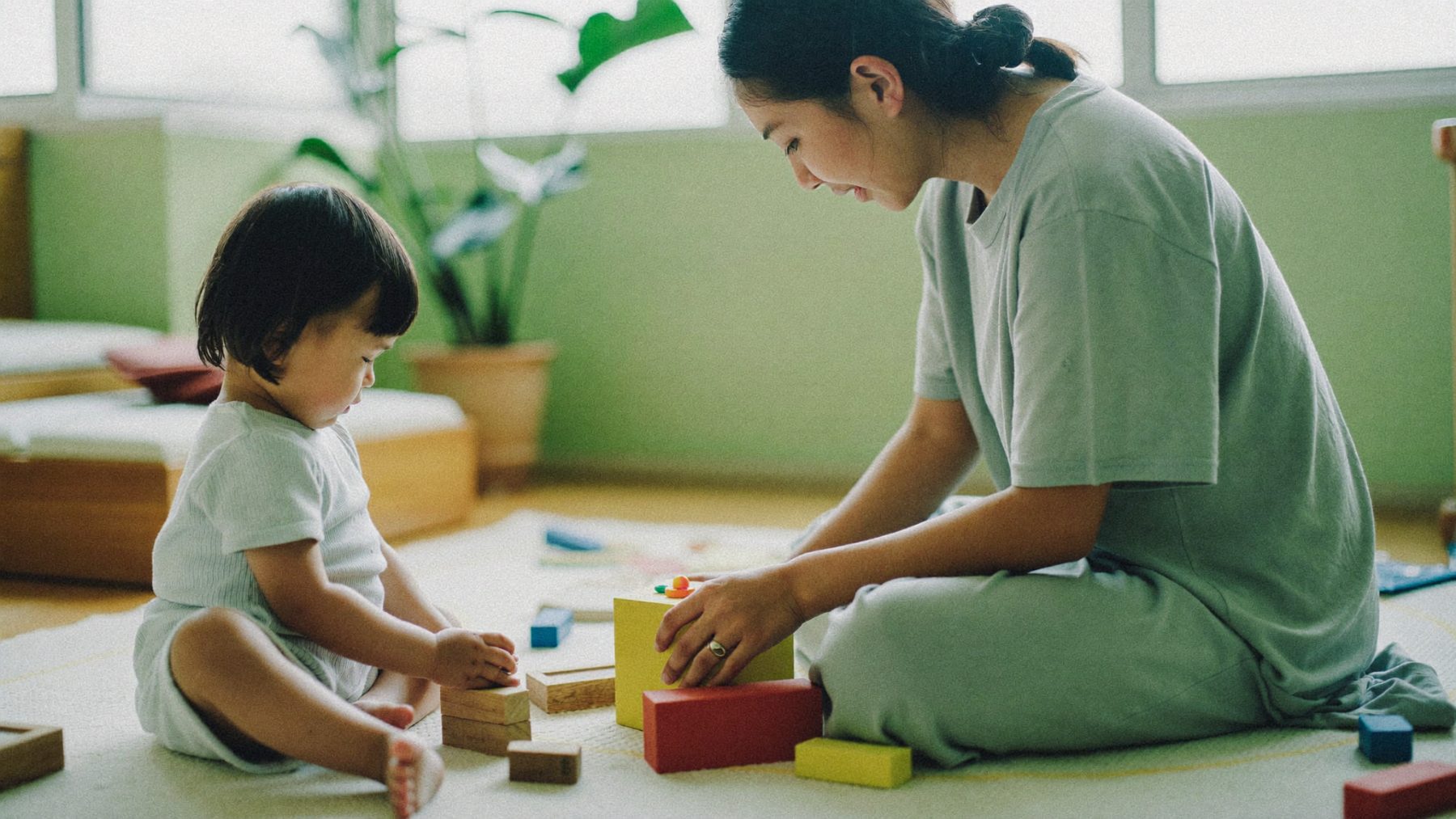 A parent and young child playing with wooden blocks together in a bright child therapy room