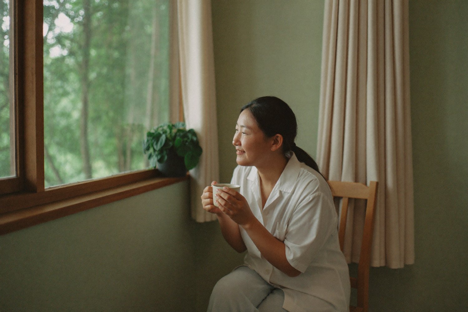 Person sitting quietly by a window with a warm drink in morning light