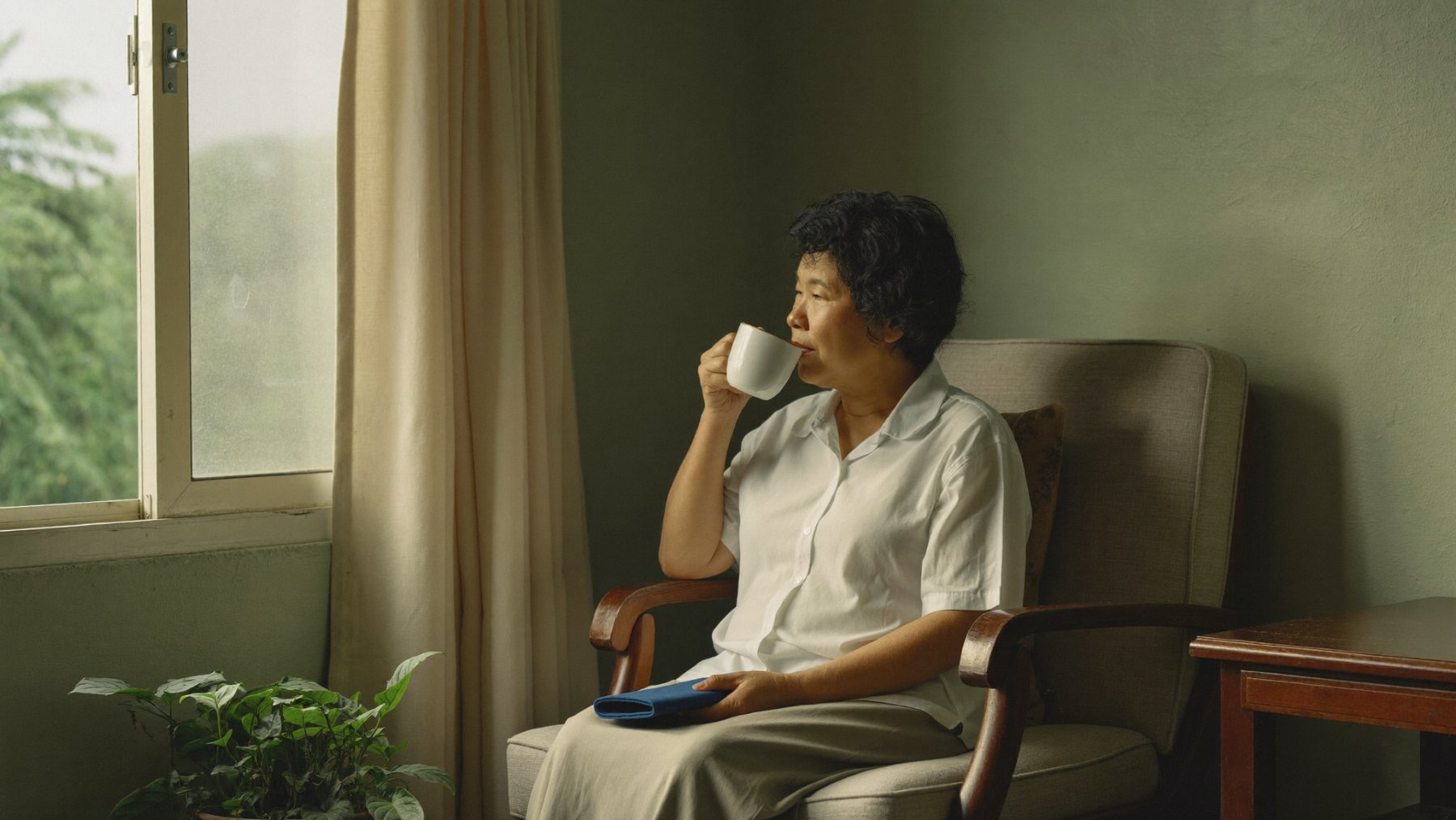 Woman sitting quietly by a window with a warm drink during grief counselling support in Petaling Jaya