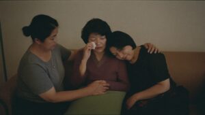 Three women sitting close together on a sofa, one crying while the others comfort her