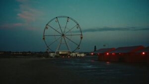 An empty fairground at dusk with a still ferris wheel silhouetted against a fading sky
