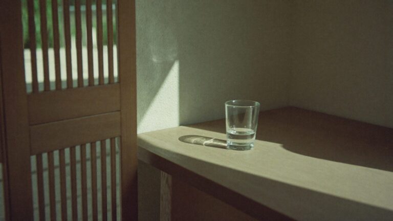Bands of sunlight and shadow falling across a wall, with a glass of water refracting the light