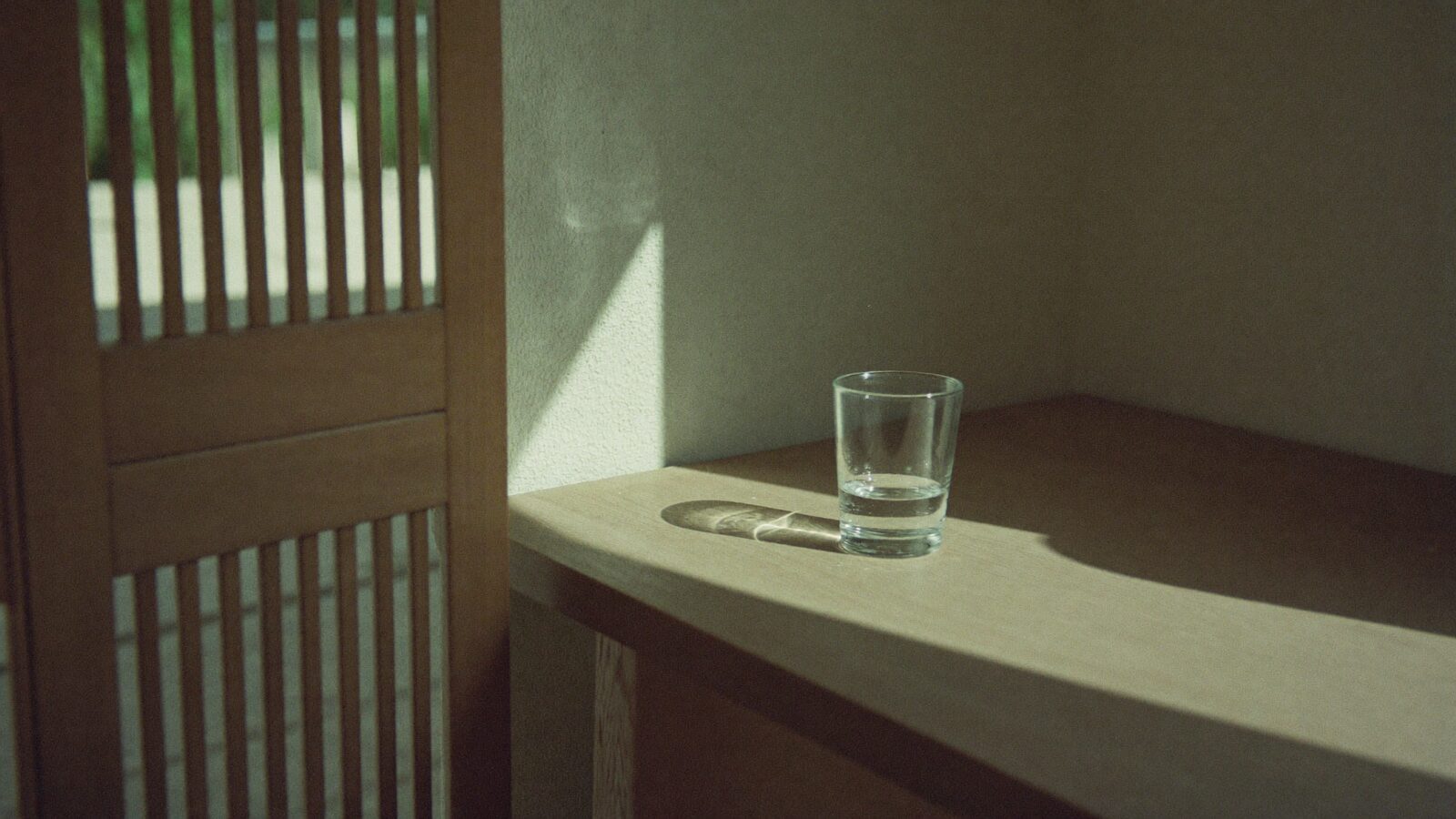 Bands of sunlight and shadow falling across a wall, with a glass of water refracting the light