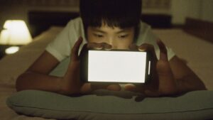 一名青少年在夜里专注地用手机玩游戏