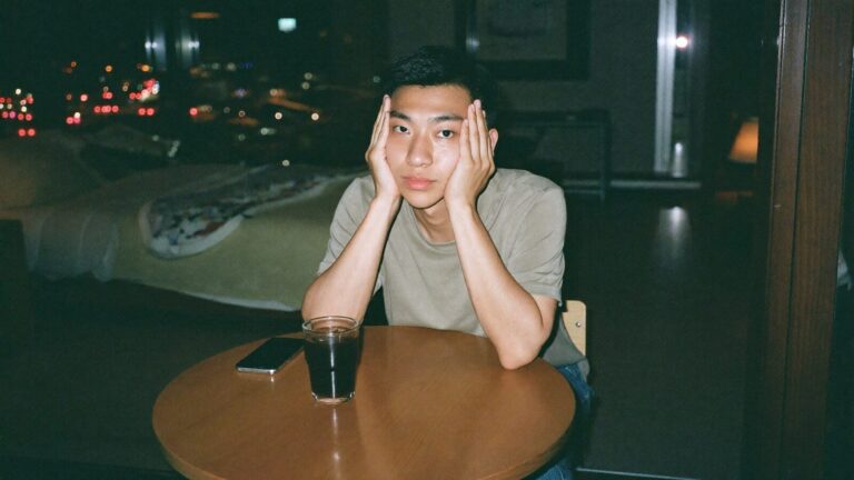 一名男子深夜坐在餐桌前双手撑头，手机倒扣在旁