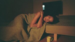 A woman curled under a blanket on a sofa watching television in the evening