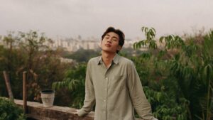 A young man standing calmly on a rooftop garden with his face lifted to the warm sky