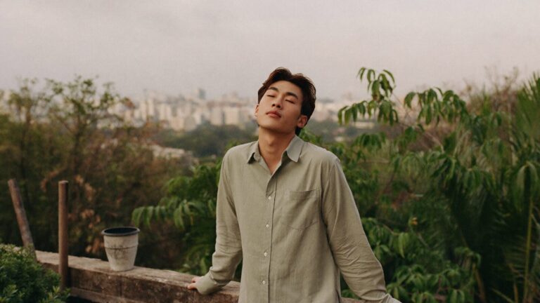 A young man standing calmly on a rooftop garden with his face lifted to the warm sky