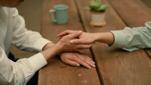 One pair of hands held gently between two others on a table, a gesture of steady support