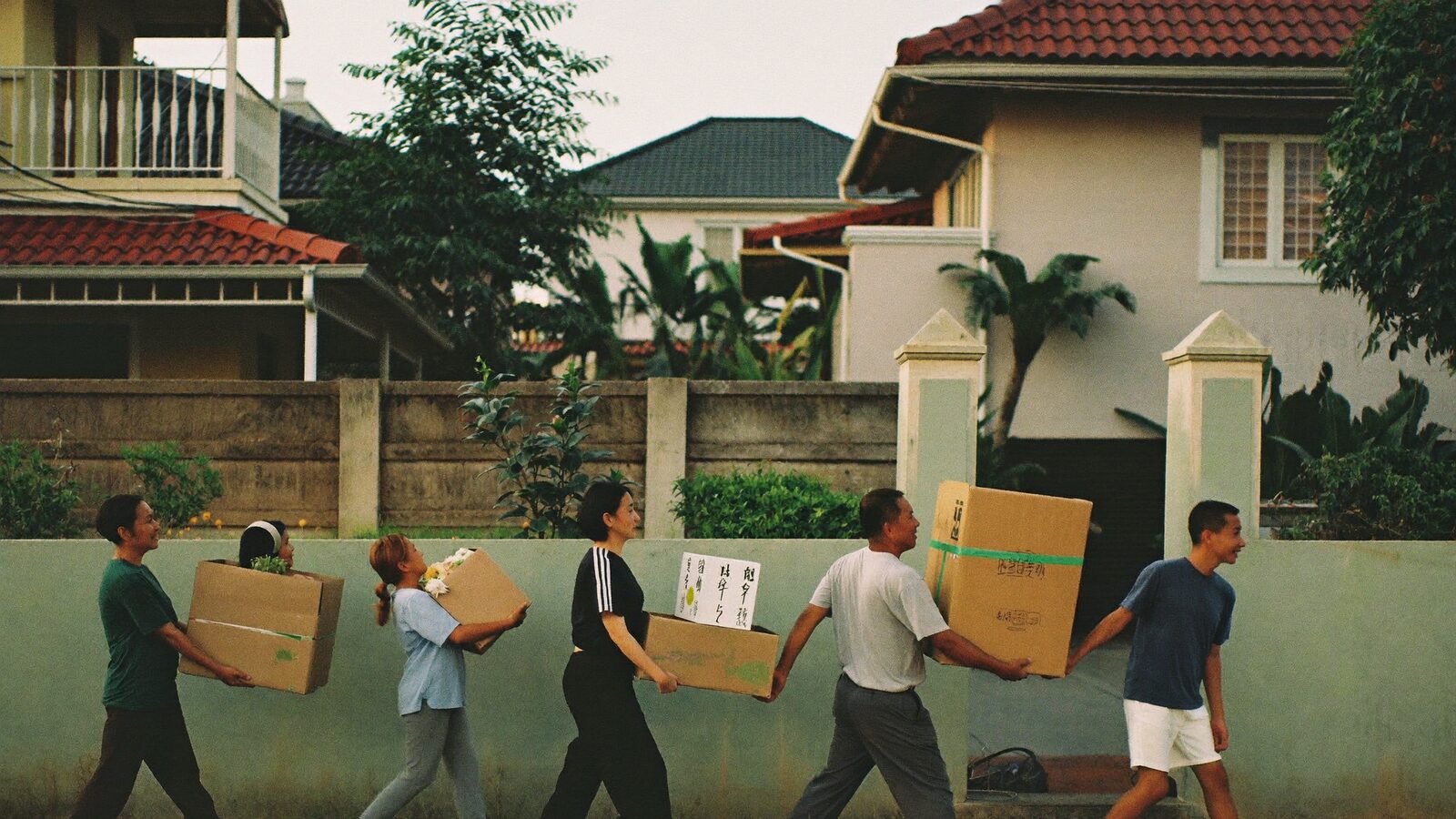 Neighbours passing boxes of groceries hand to hand along a fence in a Malaysian neighbourhood