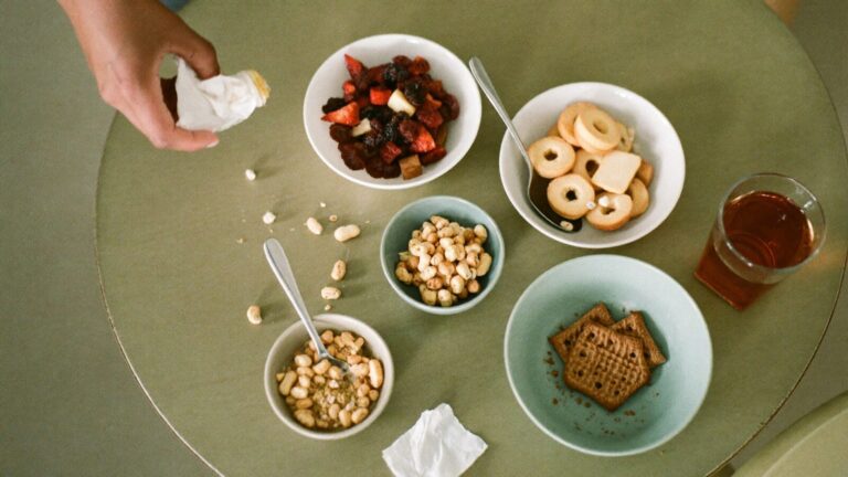 Bowls of nuts, crackers and dried fruit spread across a coffee table with a hand reaching in