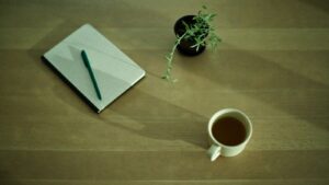 A closed notebook, pen and cup of tea on a desk, set up for a DASS-21 self-assessment