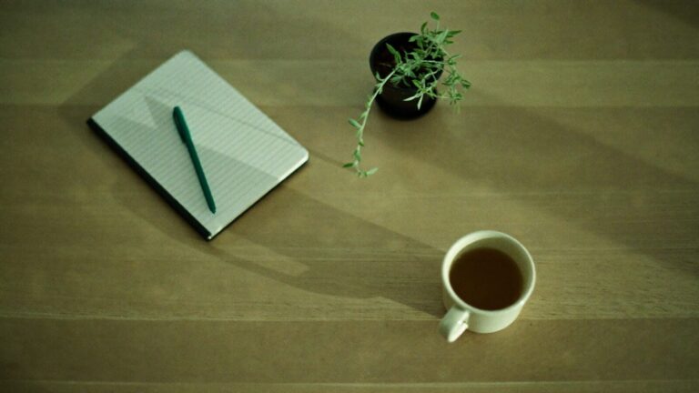 A closed notebook, pen and cup of tea on a desk, set up for a DASS-21 self-assessment