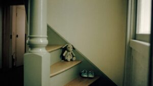 A soft toy left alone on a staircase beside a pair of small shoes in an empty hallway