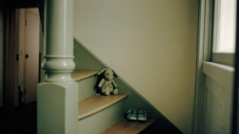 A soft toy left alone on a staircase beside a pair of small shoes in an empty hallway